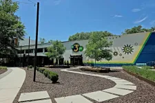 Thumbnail for Outdoor view of The 3 Spot building with curved sidewalk, trees, and decorative mural under blue sky.