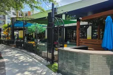 Thumbnail for Outdoor patio area with shaded seating, black metal fencing, tiled counter, and blue umbrella on a sunny day.