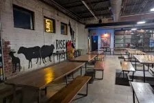 Thumbnail for Interior of a rustic industrial dining area with wooden tables, benches, and animal murals on brick walls.