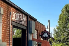 Thumbnail for Exterior view of Scofflaw Brewing Co. brick building with signage and lush greenery under clear blue sky.