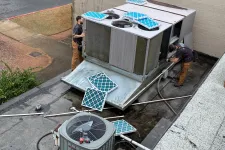 Thumbnail for Technicians installing or repairing a rooftop HVAC unit with new blue filters on a flat roof beside a building.