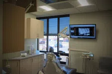 Thumbnail for Modern dental office with exam chair, dental equipment, cabinets, and X-ray displayed on wall-mounted screen.
