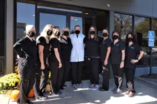 Thumbnail for Group of healthcare workers wearing black scrubs and masks standing outside a clinic entrance with autumn decorations.