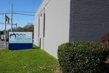 Thumbnail for Family Dentistry sign near gray brick building with green lawn and bush under clear blue sky.