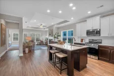 Thumbnail for Bright modern open kitchen with island, stools, stainless steel appliances, and adjoining living room with seating area.