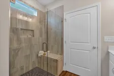 Thumbnail for Modern bathroom with glass-enclosed shower, built-in bench, beige tile walls, and white door