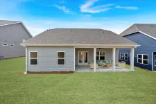 Thumbnail for Modern gray single-story house with covered patio and outdoor seating in a green lawn backyard.