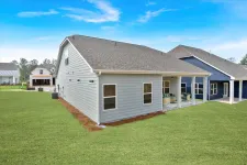 Thumbnail for Modern gray house with covered patio and green lawn under a bright blue sky in a residential neighborhood.
