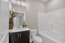 Thumbnail for Modern bathroom with dark wood vanity, white countertop, toilet, and white bathtub with shower.