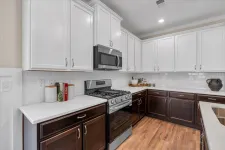 Thumbnail for Modern kitchen with white upper cabinets, dark lower cabinets, stainless steel appliances, and wood flooring.