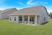 Thumbnail for Modern gray house with covered patio, outdoor furniture, and a green lawn under a blue sky.