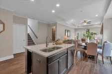 Thumbnail for Modern kitchen with island sink, dining table, upholstered chairs, and open living space with stairs in background