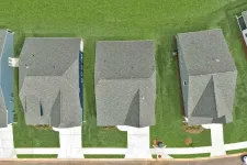 Thumbnail for Aerial view of four suburban houses with grey roofs, green lawns, and concrete driveways in a row.