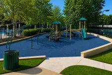 Thumbnail for Outdoor playground with blue rubber flooring, green slides, climbing structures, and surrounding trees on a sunny day