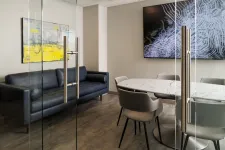 Thumbnail for Modern office meeting room with glass doors, marble table, gray chairs, black sofa, and abstract wall art.