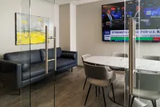 Thumbnail for Modern office meeting room with glass doors, marble table, gray chairs, black sofa, and wall-mounted TV screen.