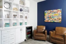 Thumbnail for Modern office lounge with brown leather chairs, white shelving, mini fridge, and colorful wall art on blue wall.