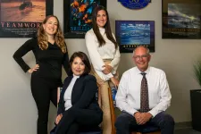 Thumbnail for Four business professionals posing in office with motivational posters and anniversary plaque on the wall.