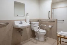 Thumbnail for Accessible bathroom with safety rails, wall-mounted sink, toilet with support arms, and a walk-in shower with grab bars.