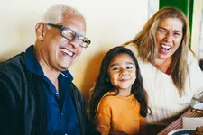 Thumbnail for Joyful multigenerational family laughing together at a meal indoors with warm natural light and cozy atmosphere
