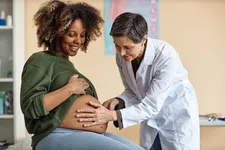 Thumbnail for Pregnant woman smiling as doctor examines her baby bump in a medical office during prenatal checkup.