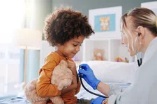 Thumbnail for Doctor using stethoscope to check a smiling child's heartbeat while the child holds a teddy bear in a cozy room.