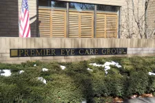 Thumbnail for Sign for Premier Eye Care Group on a brick wall with American flag and green shrubs with patches of snow.