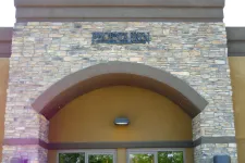 Thumbnail for Stone facade and arched entrance of Phoenix Skin Dermatology clinic with glass doors reflecting trees.