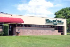 Thumbnail for Exterior view of Watson Clinic building with red awning and green lawn under a partly cloudy sky.
