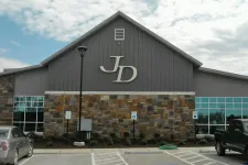 Thumbnail for Building exterior with stone facade and large JD logo above parking lot with cars and handicap spaces.