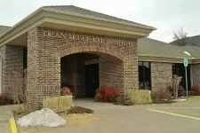 Thumbnail for Brick building entrance of Dean McGee Eye Institute with landscaping and handicap parking sign.