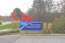 Thumbnail for Henry Ford Medical Center sign with autumn trees and foliage in the background near a roadside.
