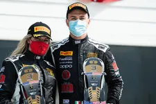 Thumbnail for Two masked race car drivers in black suits holding third-place trophies and wearing Pirelli caps on a racetrack.