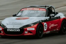 Thumbnail for Red, white, and black Mazda race car number 16 speeding on a racetrack with sponsor logos visible