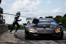 Thumbnail for Race car driver exits Lamborghini pit stop during motorsport event under partly cloudy sky.