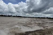 Thumbnail for Empty sandy construction site under a cloudy sky near residential houses with visible tire tracks.