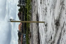 Thumbnail for Wooden pole with mounted devices on sandy ground near residential houses and cloudy sky