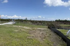Thumbnail for Cleared construction site with grassy foreground, dirt patches, machinery, and blue sky with clouds.