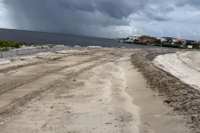 Thumbnail for Construction site by the water with sandy terrain and heavy tire tracks under stormy cloudy sky.