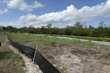 Thumbnail for Construction site barrier fencing separates disturbed soil from grassy area under a blue sky with clouds.