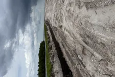 Thumbnail for Construction site with excavated trench, sandy ground, and cloudy sky over a green landscape.