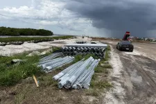 Thumbnail for Stacks of metal pipes and construction materials on a dirt road with storm clouds approaching and vehicles nearby