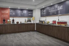 Thumbnail for Modern breakfast buffet area with waffle makers, cereal dispensers, and wooden cabinets in a clean, spacious room.