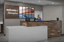 Thumbnail for Reception desk at Hampton hotel with a friendly staff member and welcome sign featuring a pier over water.