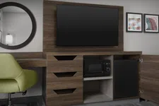 Thumbnail for Modern hotel room corner with wood TV stand, mounted flat-screen TV, microwave, mini fridge, green chair, and wall art.