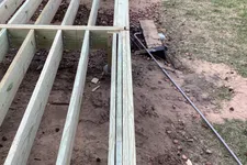 Thumbnail for Wooden deck frame construction in progress on a backyard with grass and a walkway visible.