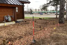 Thumbnail for Shovel standing upright in prepared soil beside a wooden log cabin with commercial buildings in background