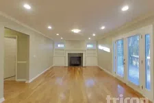 Thumbnail for Spacious empty living room with hardwood floors, fireplace, built-in shelves, and large windows with glass doors.