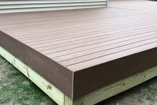 Thumbnail for Newly constructed wooden deck with composite brown decking boards next to a beige house exterior.