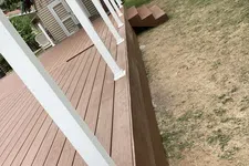 Thumbnail for New brown wooden deck with white railing posts and small stairs leading to a backyard with patchy grass.